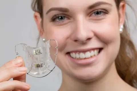 Uśmiechnięta dziewczyna trzyma przezroczysty, wieloczynnościowy aparat dentystyczny.