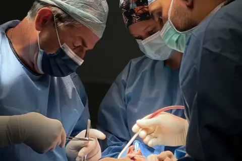 Chirurdzy w maseczkach i fartuchach wykonują skomplikowaną operację. Widać narzędzia chirurgiczne i fragment twarzy pacjenta. To zabieg osteotomii żuchwy.