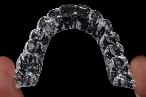 Przezroczysty aparat Invisalign, trzymany palcami, z widocznymi indywidualnymi nakładkami na zęby.