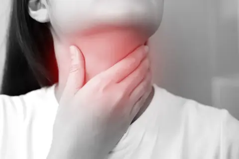 Dłoń obejmuje zaczerwienioną szyję, wskazując na ból i potencjalne objawy anginy Ludwiga.