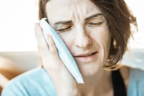 Kobieta z bólem przykłada zimny okład do policzka, być może z powodu torbieli.
