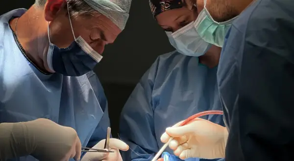 Chirurdzy w maseczkach i fartuchach wykonują skomplikowaną operację. Widać narzędzia chirurgiczne i fragment twarzy pacjenta. To zabieg osteotomii żuchwy.